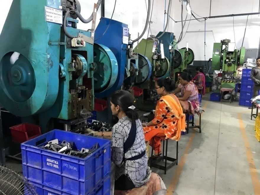 Workers operating power press machines for sheet metal automotive parts production.